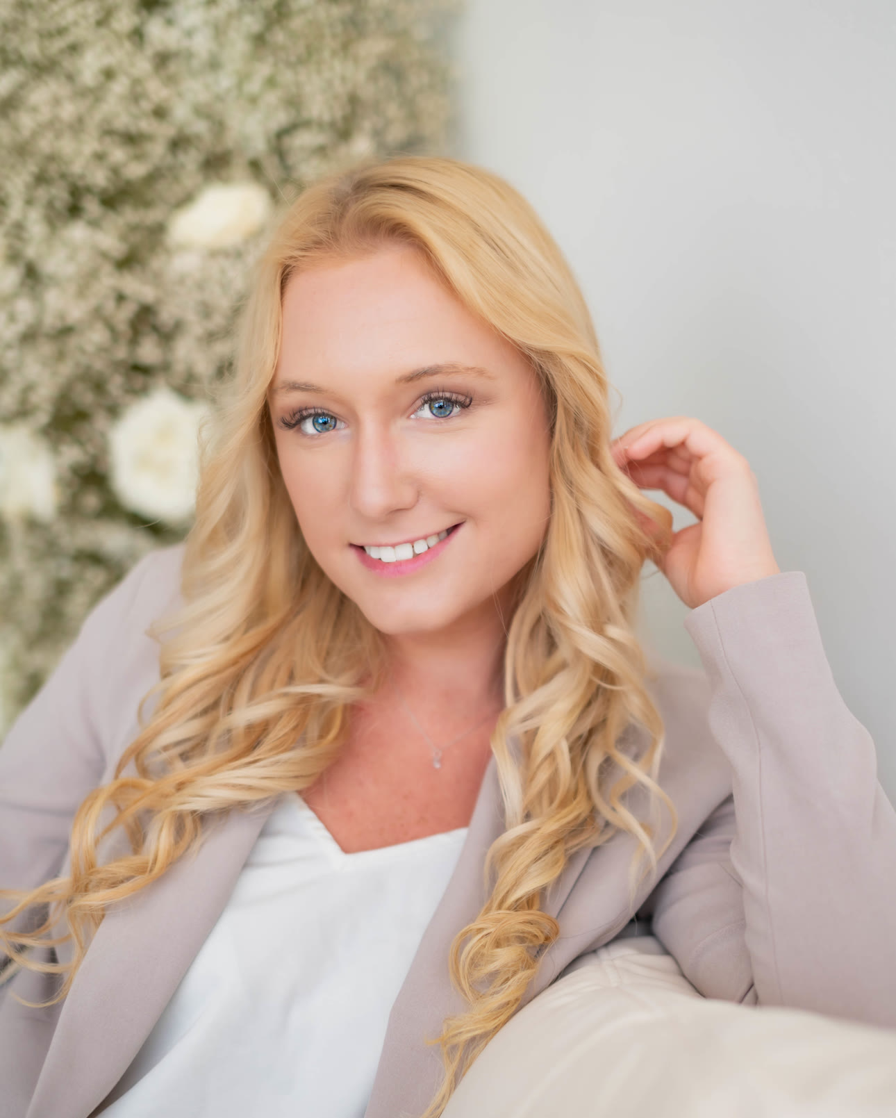 Hannah Lee, founder of Synovial Marketing, smiling and tucking her hair back, seated on a cream sofa
