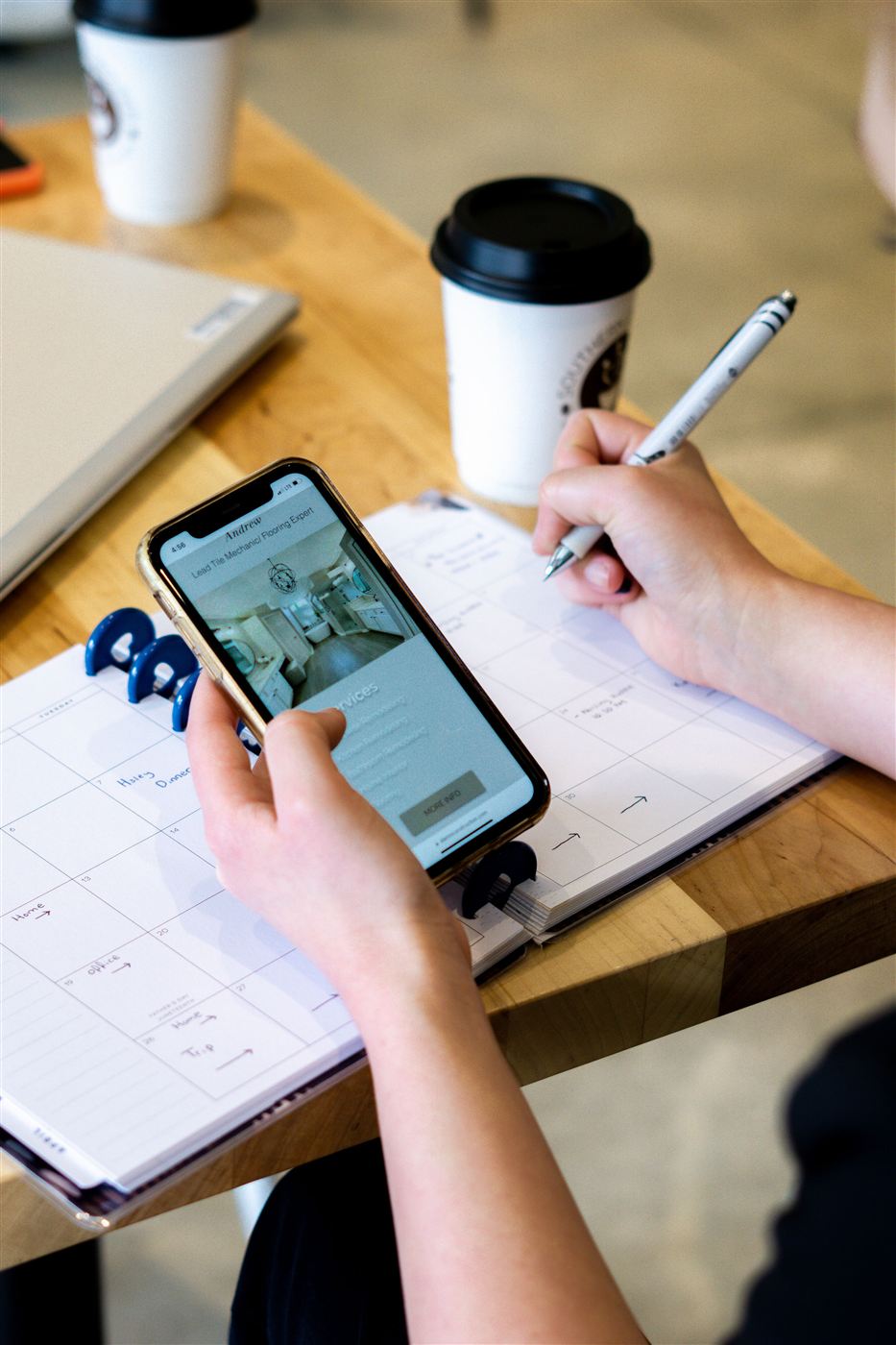 A phone in hand above an open planner and coffee