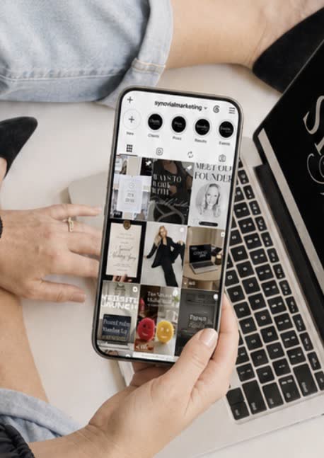 The Synovial Marketing Instagram profile open on a phone beside a laptop
