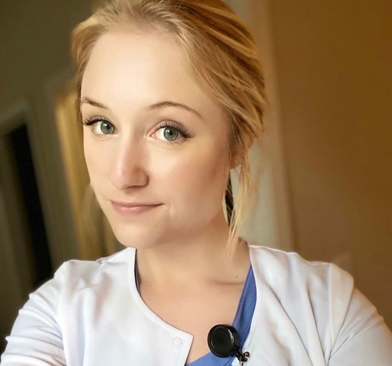 Hannah in her white coat over scrubs, a selfie from her clinic days